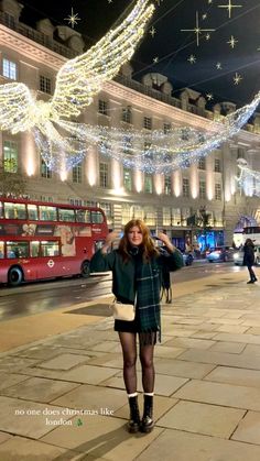 a woman standing in front of a red double decker bus on a city street at night