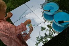 a little boy sitting at a table with two blue drinks in front of him on the grass