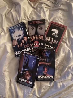 five scream movie posters laying on top of a white sheet covered bed with the covers pulled down