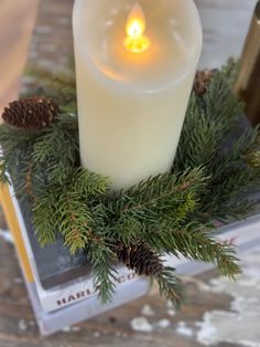 a lit candle sitting on top of a book next to pine cones and candlesticks