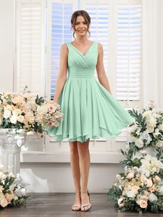 a woman standing in front of flowers wearing a green bridesmaid dress and heels