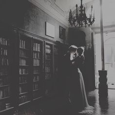 a man and woman standing next to each other in front of bookshelves with chandeliers