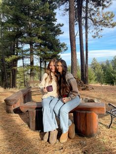 two young women sitting on a bench in the woods with their arms around each other