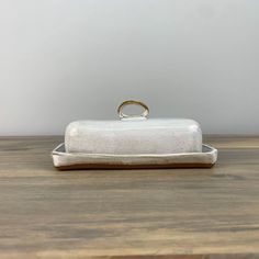 a white box sitting on top of a wooden table with a gold ring in it