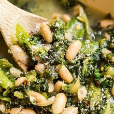 broccoli and white beans are mixed together in a pot with a wooden spoon