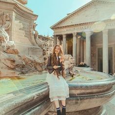 a woman sitting on the edge of a fountain in front of a building with columns