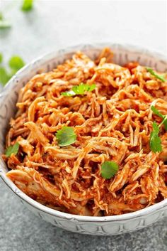 a white bowl filled with shredded meat and garnished with cilantro leaves