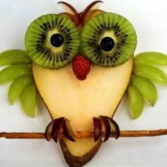 a kiwi bird made out of fruit sitting on top of a wooden stick with leaves