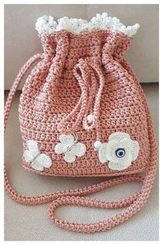 a pink crocheted purse with white flowers on the front and side, sitting on a couch