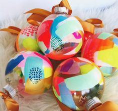 four colorful glass ornaments are on a white furnishing area with ribbon around them