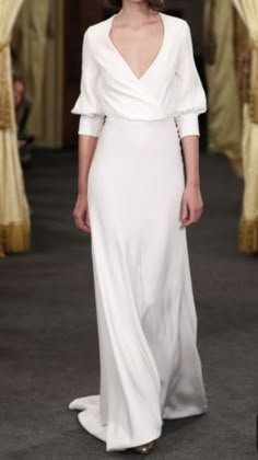 a woman walking down a runway wearing a white dress with long sleeves and an open back