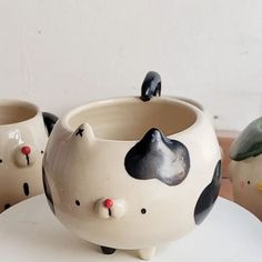 three ceramic cats sitting on top of a white table next to two small pots with faces painted on them