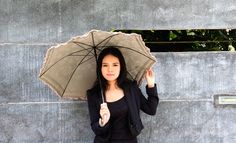 a woman holding an umbrella over her head while standing next to a concrete wall with trees in the background