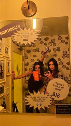 two women standing in front of a mirror holding up their cell phones and pointing at them