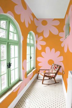 a chair sitting in front of a window next to a wall with flowers painted on it