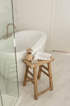 a white bath tub sitting next to a wooden stool