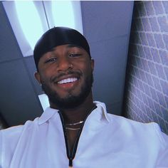 a man in a white shirt and black hat smiles at the camera while sitting on an airplane