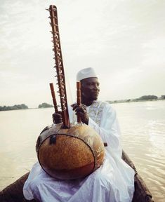 a man sitting on the back of a boat with musical instruments in his hand and wearing a white turban