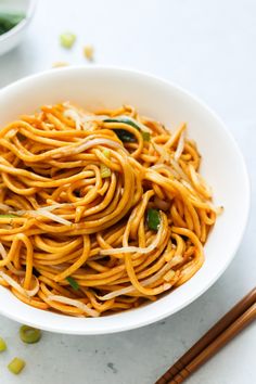 a white bowl filled with noodles next to chopsticks