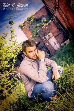 a man sitting in the grass with his hand on his chin and looking at the camera