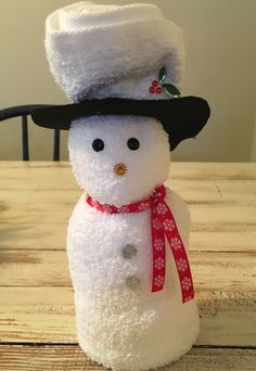 a stuffed snowman wearing a black hat and scarf on top of a wooden table