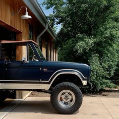 a large blue truck parked in front of a building next to a tree and shrubbery