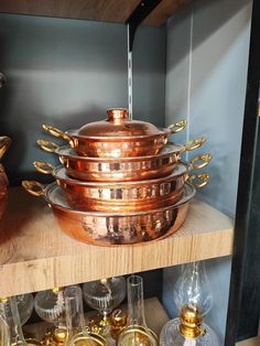 a stack of copper pots and pans sitting on top of a wooden shelf