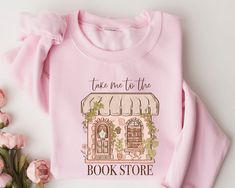 a pink shirt with the words take me to the book store on it and flowers