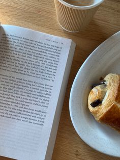 a croissant on a plate next to an open book