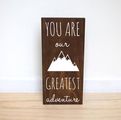 a wooden sign that says you are our greatest adventure with mountains in the background on a wood floor