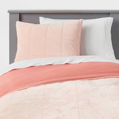 a bed with pink and white comforters on top of it, next to a gray headboard