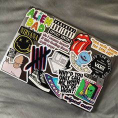 a laptop covered in stickers on top of a gray sheet with writing and pictures