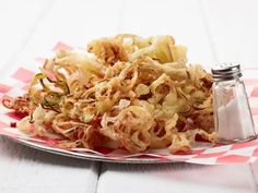 a plate topped with fried onions next to a salt shaker on top of a checkered table cloth