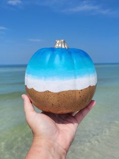 a hand holding a painted pumpkin on the beach