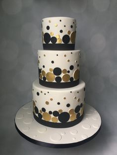 a three tiered cake with black and gold polka dots on the bottom, sitting on top of a white plate