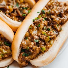 three hot dogs on buns covered in chili and relish sitting on a plate