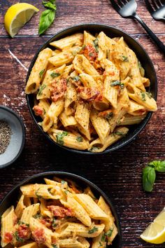 two bowls filled with pasta on top of a wooden table next to lemon wedges