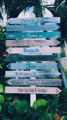 a wooden sign with many different signs on it in front of some plants and trees