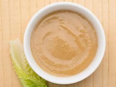 a white bowl filled with brown liquid next to a green leafy lettuce