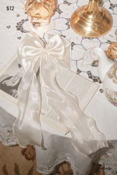 a table topped with an open book next to two candles and a teapot on top of a table cloth