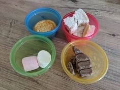 four bowls with different types of food in them on a wooden table, including marshmallows and crackers