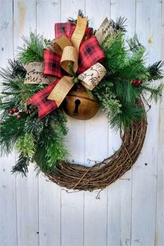 a christmas wreath hanging on the side of a white wooden wall with bells and evergreen leaves