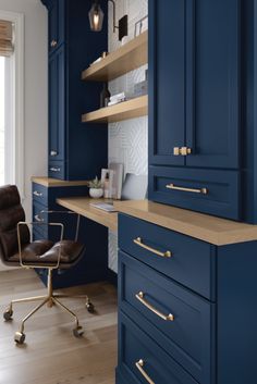 a kitchen with blue cabinets and gold pulls on the handles, along with a brown leather chair