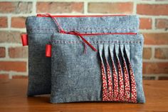 the zippered pouch is made from gray fabric and has red thread on it's side