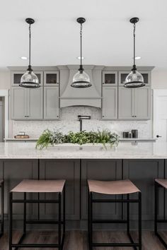 three lights hanging from the ceiling above a kitchen island with stools and plants on it