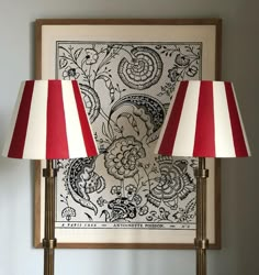 two red and white lamps sitting on top of a wooden table next to a painting