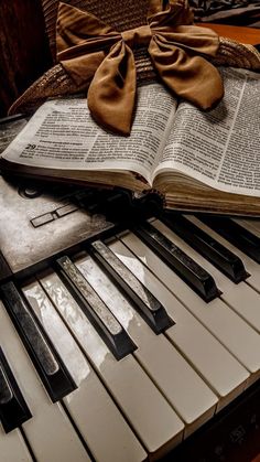 an open book sitting on top of piano keys with a bow around it's neck