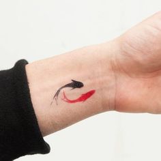 a woman's hand with a red and black fish tattoo on her left wrist