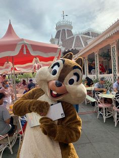 a person dressed as chip the chip standing in front of an outdoor dining area with tables and umbrellas