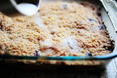 a glass baking dish filled with blueberry cobbler crumbs and milk being poured into it